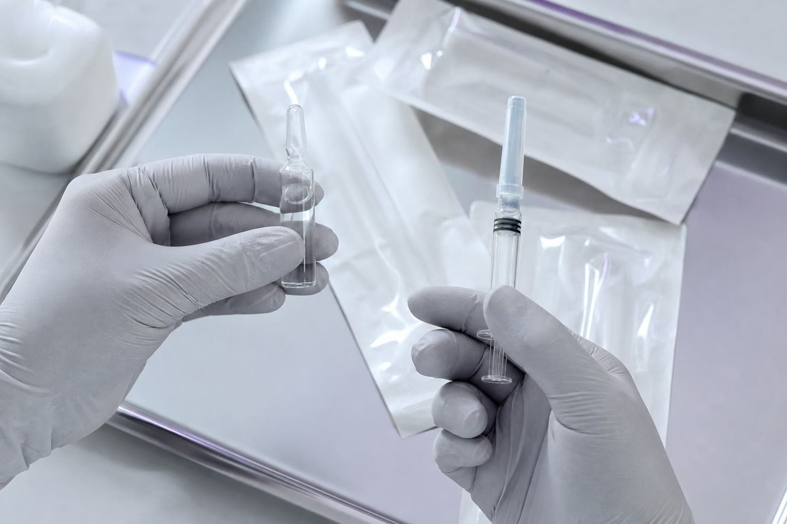 Gloved clinician hands preparing a glass ampoule and capped syringe on a sterile tray